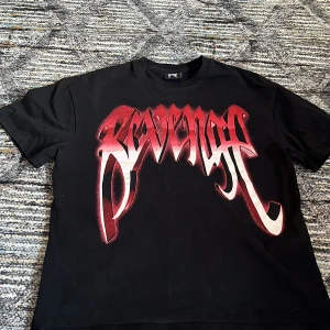 Revenge svart t shirt - En fet svart tischa med röd text o röd dödskalle print på ryggen, med märket Revenge. Tischan kommer med förpackningen som den köptes med.