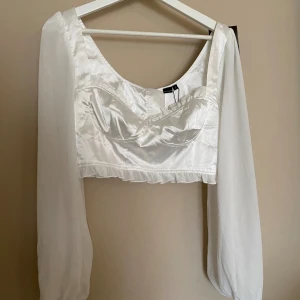 Vit blus med volang detaljer - Vit blus med satin kropp och lätt genomskinliga armar. Definierade kupor och volang detaljer. Stor i storleken.