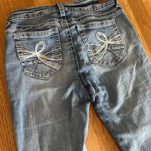 Lågmidjade jeans med mönster på fickor - Jeans från märket Wallflower. De är lågmidjade och bootcut, inga defekter. De har fina detaljer längs med benen, midjan och på fickorna. Storlek står ”0” men jag själv har storlek 34/36 eller även 26 och de passar mig fint. NYPRIS 1940kr!!