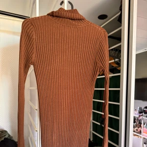 Stickad tajt brun klänning - Säljer denna fin stickade klänning då den aldrig kommit till användning, klänningen är med en liten polokrage och är i storlek M/L men skulle nog mer säga att den passar S/M 
