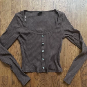 Brun tröja med knappar - En aldrig använd brun långärmad tröja från bikbok med knappar som går att knäppa upp i storlek Xs
