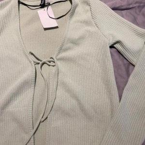 Ljusgrön knytkofta - Ribbad ljusgrön kofta med snöre. Perfekt till sommaren. Helt ny med prislapp, oanvänd.