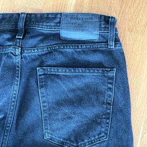Svarta jeans från Jack & Jones - Svarta jeans från Jack & Jones.  Femficksdesign med knappar som stängning framtill. Mycket fint skick. 