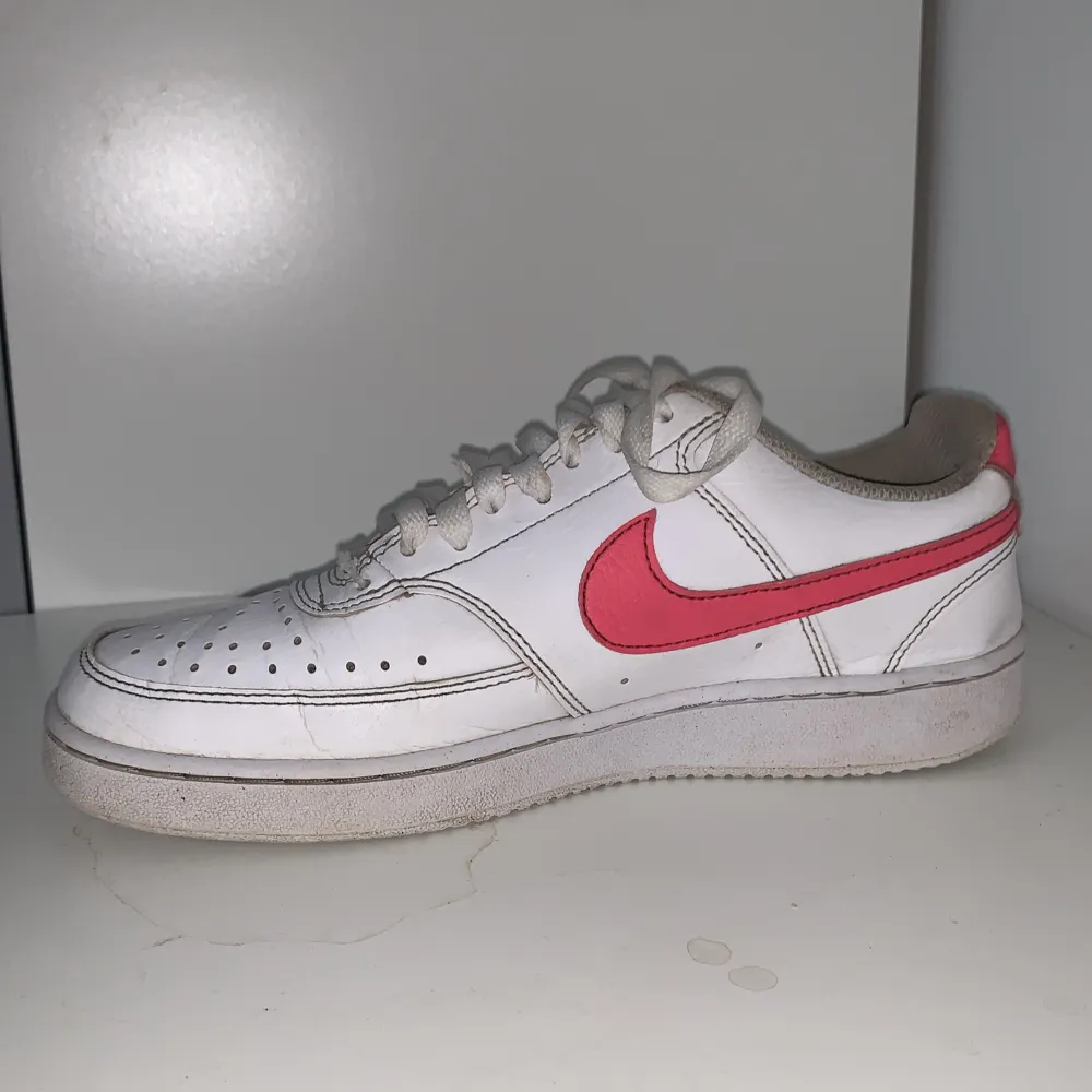 Vita Nike skor med rosa nikemärke. Skorna är i bra skick använda 1 säsong men har blivit lite nertrampade vid hälen, men inget jag märker av!. Skor.