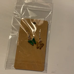  Fjärilsörhängen - Ett par fjärilsörhängen med en gul fjäril och en grön. Är aldrig använda, och ligger som ni ser kvar i förpackningen.