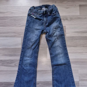 Blå jeansbyxor - Ett par blå jeansbyxor med elastisk midja och broderade bakfickor. Byxorna har en något utsvängd passform. Från Polarn O Pyret i storlek 134