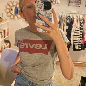 Grå t-shirt från Levi's - En grå t-shirt från Levi's med röd logotyp på bröstet. T-shirten har korta ärmar och en normal passform😁😁🙌💗