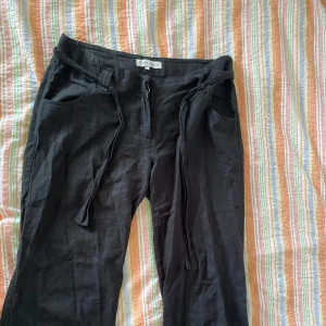 Svarta byxor från Fresh Spirit - Ett par svarta byxor från Fresh Spirit med dragsko i midjan och dragkedja. Byxorna har fickor både fram och bak. egen fixad dragkedja, kan behöva sys på ny knapp för att dragkedjan ska hållas uppe! inget som syns när bältet är knutit :)