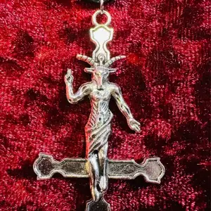 Svart halsband med inverterat kors i form av Baphomet, ibland kallad bockguden från Mendez.   Amuletten är cirka 4 cm lång och 2,7 cm bred.   Halsbandet i konstläder är 44 cm långt med 5 cm extra att justera med.   Ovanligt och nytillverkat av mig. 