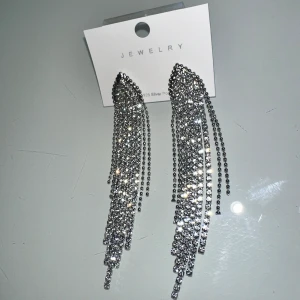 Örhängen  - silvrigt örhänge med klara stenar i glas som påminner om 💎 får smycket att gnistra och glittra. Detta smycke är pläterade med ett lager rhodium vilket ger smycket en skyddande yta och är extra skonsamt mot huden.