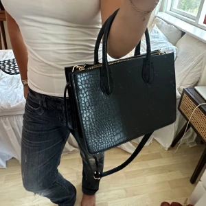 svart handväska med ormskinn mönster - svart handväska i fejk ormskinn. den har även ett längre band så att man kan bära den över axeln (bandet går att ta av). från hm och aldrig använd. utmärkt skick! köpt för 499 kr