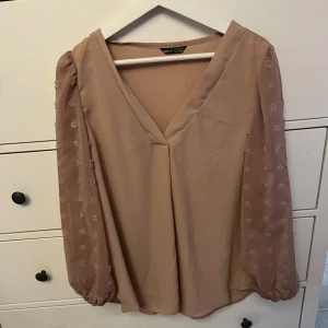 Rosa  blus från Shein - En elegant rosa blus från Shein med långa ärmar och v-ringad hals. Ärmarna är dekorerade med små blommiga mönster och har elastiska muddar vid ärmslut. 
