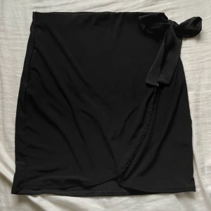 Svart minikjol med rosett - Jätte gullig svart kort kjol med en justerbar knyt. Säljer då den är lite för stor för mig. Jätte gullig till sommaren💕 