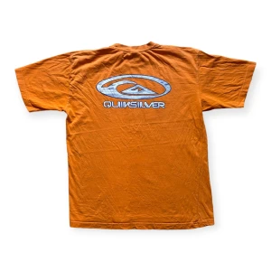 Vintage Quiksilver T-shirt med tryck på - Snygg orange Quiksilver t-shirt med tryck på både fram och bak. Står storlek M på lappen men passar mer som L.  En aning urtvättad och har nån liten fläck på sig samt nån missfärgning som knappt syns, se bilder. Annars i fint skick!