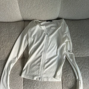 Vit ribbad tröja med dragkedja - En vit ribbad tröja med dragkedja framtill. Tröjan har långa ärmar och en åtsittande passform.