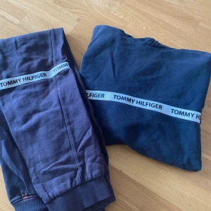Mörkblå hoodie från Tommy Hilfiger - En mörkblå hoodie från Tommy Hilfiger med ett band med texten 'Tommy Hilfiger' runt bröstet. Hoodien har långa ärmar och en huva.