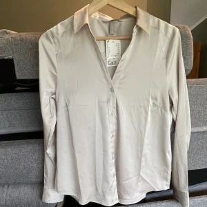 Beige satinblus  - Helt ny v- ringad beige blus från H&M. Storlek 38, dock liten i storlek… Endast  provad, prislappen kvar. Skriv för fler bilder. 