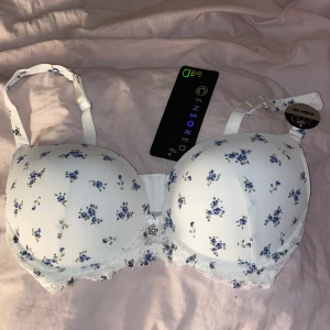 Bh - Vit bh med push upp. Blått blommigt mönster, litet silvrigt hänge med en blomma i spets runt om. Storlek 80D.