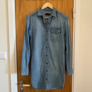 Jeansskjorta, strl XS - En fin jeansskjorta/klänning från JC av 100% bomull som är normal i storleken. Perfekt för en ledigare stil. Är i oanvänt skick, då ägaren till plagget inte hann använda det innan hon växte ur det.  Frågor? Skicka ett dm! 