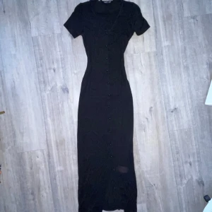 Svart långklänning - Boohoo- svart kortärmad långklänning med svarta knappar, oanvänd. Endast testad. 