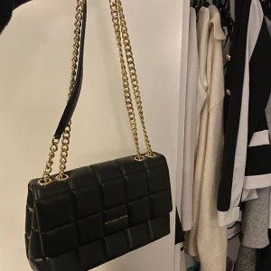 Michael Kors - Michael Kors väska i färgen svart. Medelstor o h rymlig. Så fin och elegant med gulddetaljer. Tveka inte höra av er vid ytterligare funderingar 