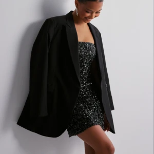 Bandeau paljettklänning - Svart paljettklänning, perfekt vid fest. Säljer då den tyvärr är för stor för mig. Vet tyvärr inte vad det är för storlek då lappen är avklippt. Men skulle säga M-L. Har en liten slits nedtill. Nypris 400kr.