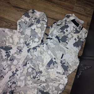 Jacka och tillhörande täckbyxor  - Vit kamouflage skid & snowboardkläder, jacka storlek S med till hörande byxor storlek M.  Slitage på baksida byxor vid hälarna(har gått på dom) lätt att laga om man orkar, inget som stör funktionen eller syns i övrigt mycket fint skick. 