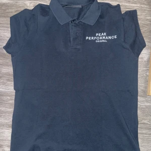Pikétröja från Peak Performance i storlek M - Säljer en marinblå pikétröja från Peak Performance i storlek M. Tröjan är i mycket bra skick och har en klassisk design med märkeslogo på bröstet. Materialet är mjukt och bekvämt.