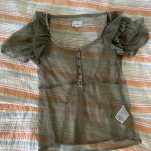 Grön blus från Noa Noa - En elegant grön blus från Noa Noa med korta puffärmar och knappar framtill. Blusen är genomskinlig och har en lös passform.