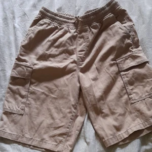 Beige shorts från H&M - Beige cargo-aktiga shorts från H&M med elastisk midja och fickor. Köpt för 2 år sedan för 200kr. 