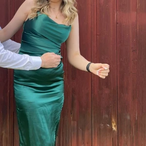 Grön satinklänning - Säljer min gröna klänning från min studentgala förra året. En grön klänning i satin imitation. Klänningen har en tight passform och når till knäna. Har en slits på vänster sida. 