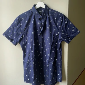 Burton London kortärmad skjorta (M) mörkblå - Oanvänd kortärmad skjorta i mörkblå med fåglar på. Märke: Burton Menswear London.  Strl M. Ordinariepris 500kr