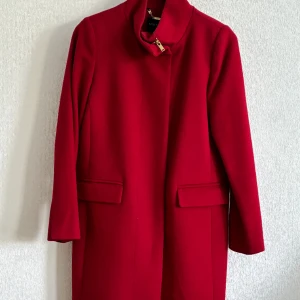 Damkappa STOCKH LM - Fin röd kappa med guld detaljer från STOCKH LM i nyskick har knappt använts, inga märken eller hål. nypris ca 1500.  50% ull, 40% polyester och 10% viskos.