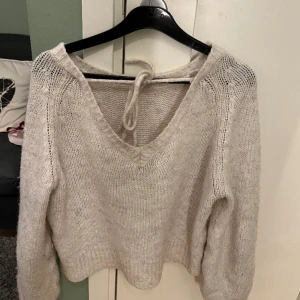 Stickad tröja med urringad rygg - En fin ulltröja med öppen rygg med knytning 💕 Inga defekter förutom att den är lite nopprig som man ser på bilden 💕 Men inget man egentligen tänker på.💕 Den är mer ljus beige än vad det framgår som på bilden 