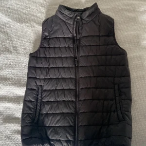 Svart Dunväst - Svartdunväst i perfekt skick. Perfekt året runt, kompletterar olika oufits väldigt bra. Fin svart dunväst för dig som vill klä dig sthlmstil, Grisch elr Laidback. Storlek S, 170/176 ifrån Everest