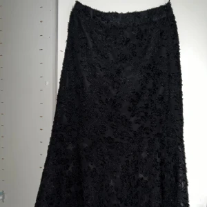 Svart kjol - Blommigt mönster. Underkjol. Resår bak. Dragkedja sida.