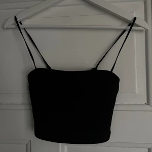 Svart topp  - Svart enkel topp från chiquelle med smala axelband, 19cm lång. Banden kan justeras. Se andra bilden för defekt band