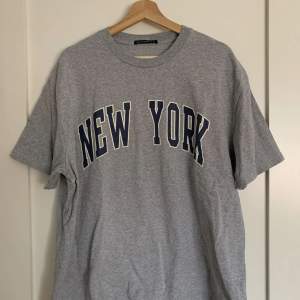 Oversized t-shirt i grått från Brandy Melville med New York-tryck. Den är i bra skick, endast använd 3-4 gånger och är one size.  Ursprungligt pris: 30$ (US-dollar) Obs: köparen står för frakten! 