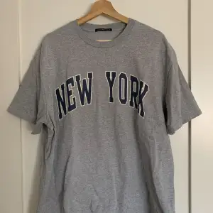 Oversized t-shirt i grått från Brandy Melville med New York-tryck. Den är i bra skick, endast använd 3-4 gånger och är one size.  Ursprungligt pris: 30$ (US-dollar) Obs: köparen står för frakten! 