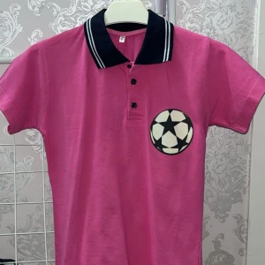 T-shirt med tryck - Rosa pikétröja med en bild av en fotboll. Kragen lutar sig åt det marinblåa hållet. Helt ny aldrig använd. Baksidan är helt rosa. Vet ej märket men det är en storlek 8. 