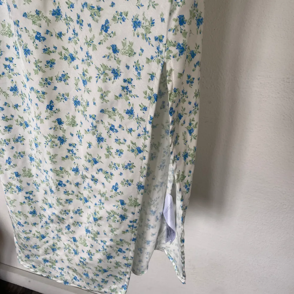 Vit långklänning med blå/gröna blommor. Justerbara linneärmar, slits nedtill samt lite ”extra” tyg vid bysten. Använd en gång, som ny.. Klänningar.