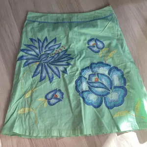 Jättefin grön kjol med insydda blommor av blå nyanser på fram och bakdelen med gula blad och fina detaljer. Jätte skönt material!  Nyttskick💗