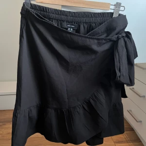 Svart omlottkjol  - Superfint omlottkjol från vero Moda som passar till alla tillfällen. Super bra skicka, endast använd några få gånger. Storlek M. Resår och knyte i midjan. Säljer pågrund av att den inte passar längre.