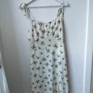 Blommig sommarklänning med volang nedtill - Dragkedja vid sidan och reglerbara axelband. Strl 40/42/L enligt lappen.