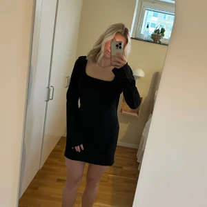 Svart klänning  - Kort klänning med öppning i ryggen. Armarna är raka/ lite vida längst ner. 