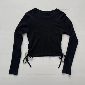 Svart snörad tröja - Svart tajt/cropped tröja med snörning i sidan! Så du kan justera hur tajt den sitter! Bortklippt tag men inga slitningar! Perfekt till fest outfit med massa smycken eller vardag med ett par jeans! 