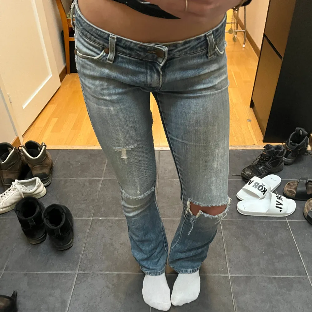 Lågmidjade ljusblå flared/ bootcut wrangler jeans med slitningar på knäna. Från tidigt 00-tal. Storlek 34/xs.  Är slitna vid en av bakfickorna och i skrevet men märks inte riktigt /påverkar inte heller passform.. Jeans & Byxor.