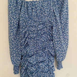 Blå sommarklänning  - En blå blommig sommarklänning i stl xs och är tajt med pösiga armar. Dragkedja på sidan finns. 
