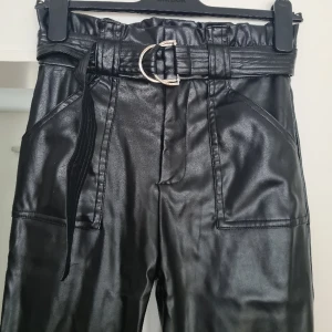 Svarta skinnbyxor  - Svarta skinnbyxor, paper bag pants. Skärp i midjan, fickor bak och fram, hög midja. Använd fåtal gånger, fint skick, normal i storleken. Kom med prisförslag 😊  Material: 45% Polyester, 55% Polyurethane.