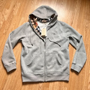 Burberry zip hoddie - Grå burberry zip up hoddie använd fåtal gånger därför 9/10 annars no flaws. Strlk L men sitter som M. Taggen följer med 